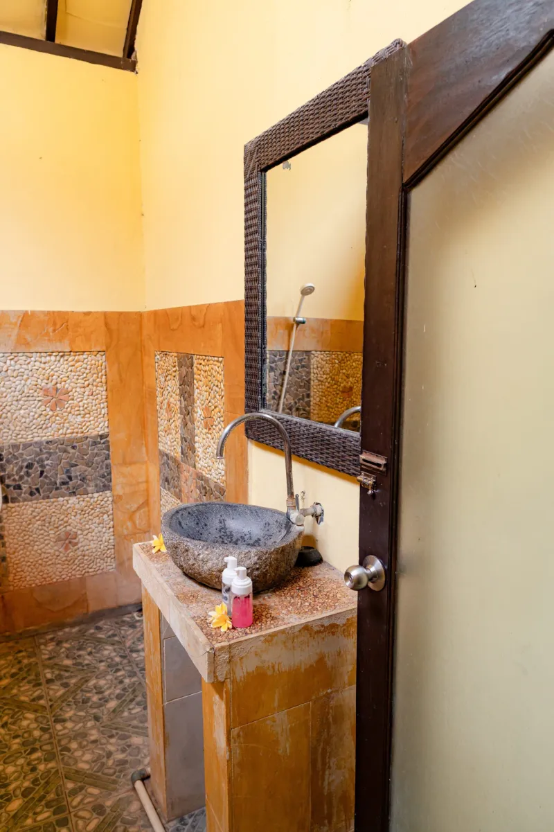 Kamar mandi rustic dengan wastafel batu dan ubin kerikil